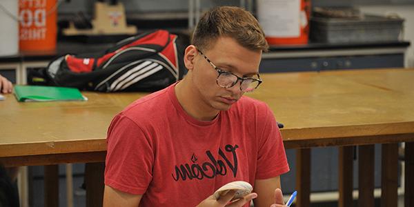 student in red shirt looking at shell